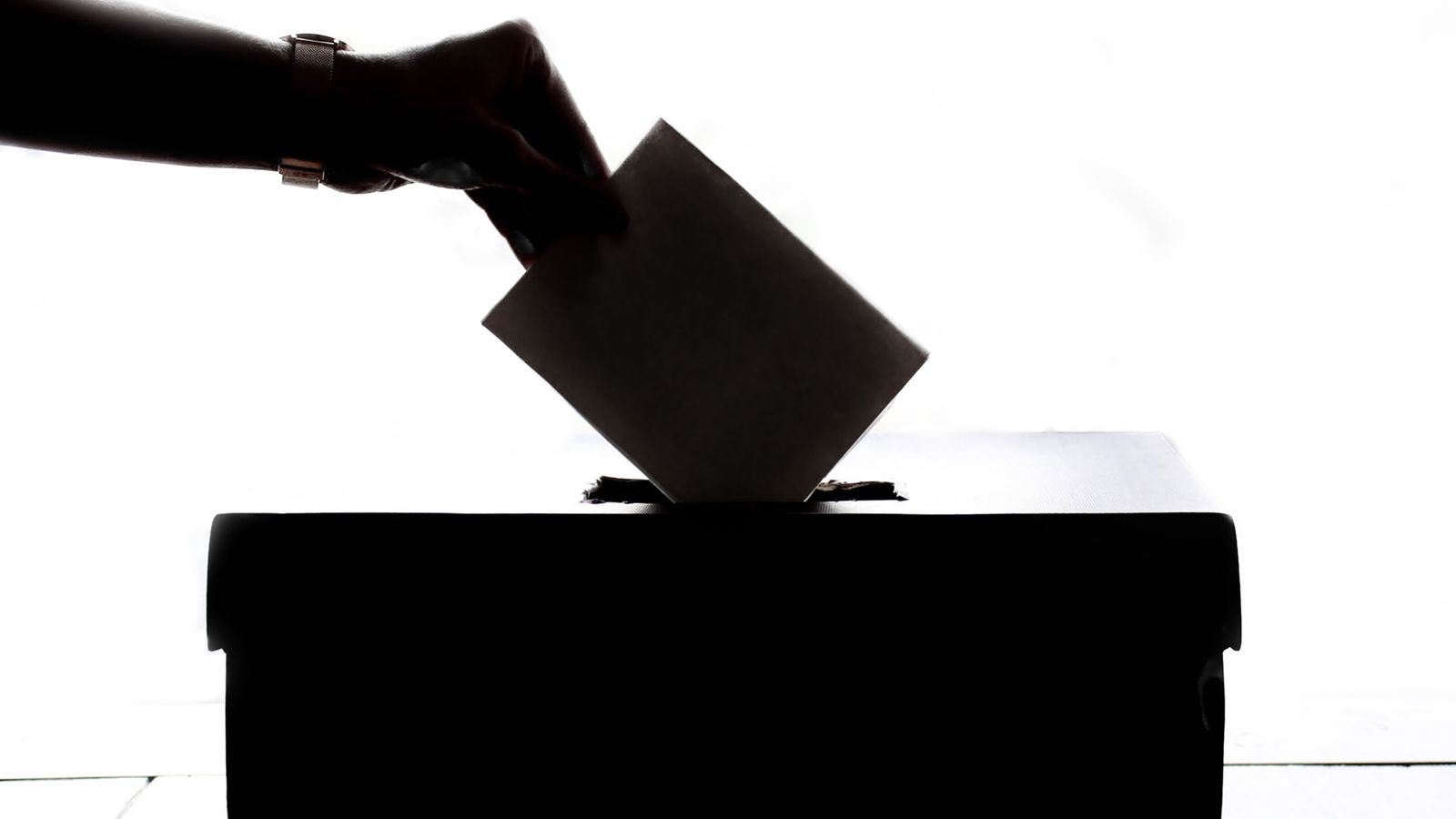 Silhouette d'une main déposant un bulletin de vote dans une urne électorale.