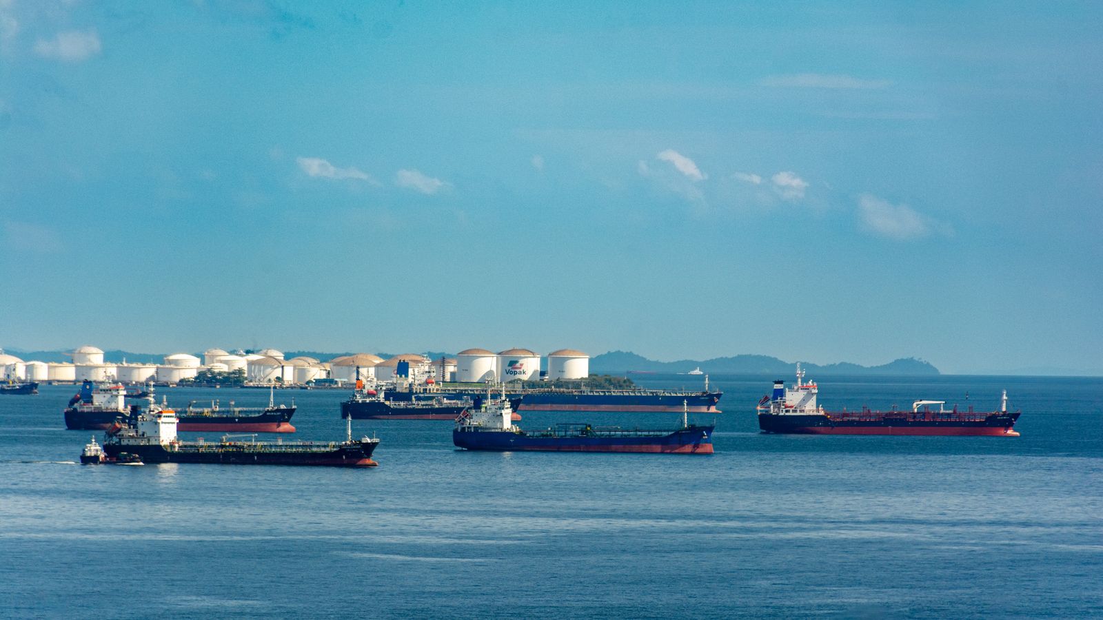 Plusieurs pétroliers à l'ancre près d'un terminal de stockage, sous un ciel bleu.