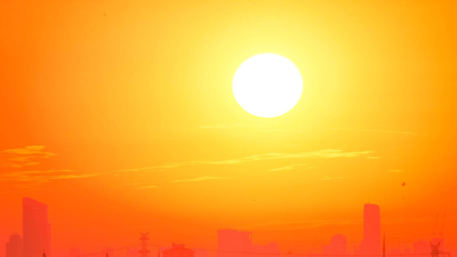 Le soleil brille intensément au-dessus des silhouettes d'une ville, dans un ciel orangé de forte chaleur.