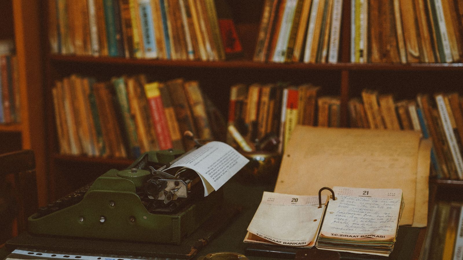 Une machine à écrire vintage posée devant une bibliothèque de livres anciens, dans une lumière chaleureuse et feutrée.