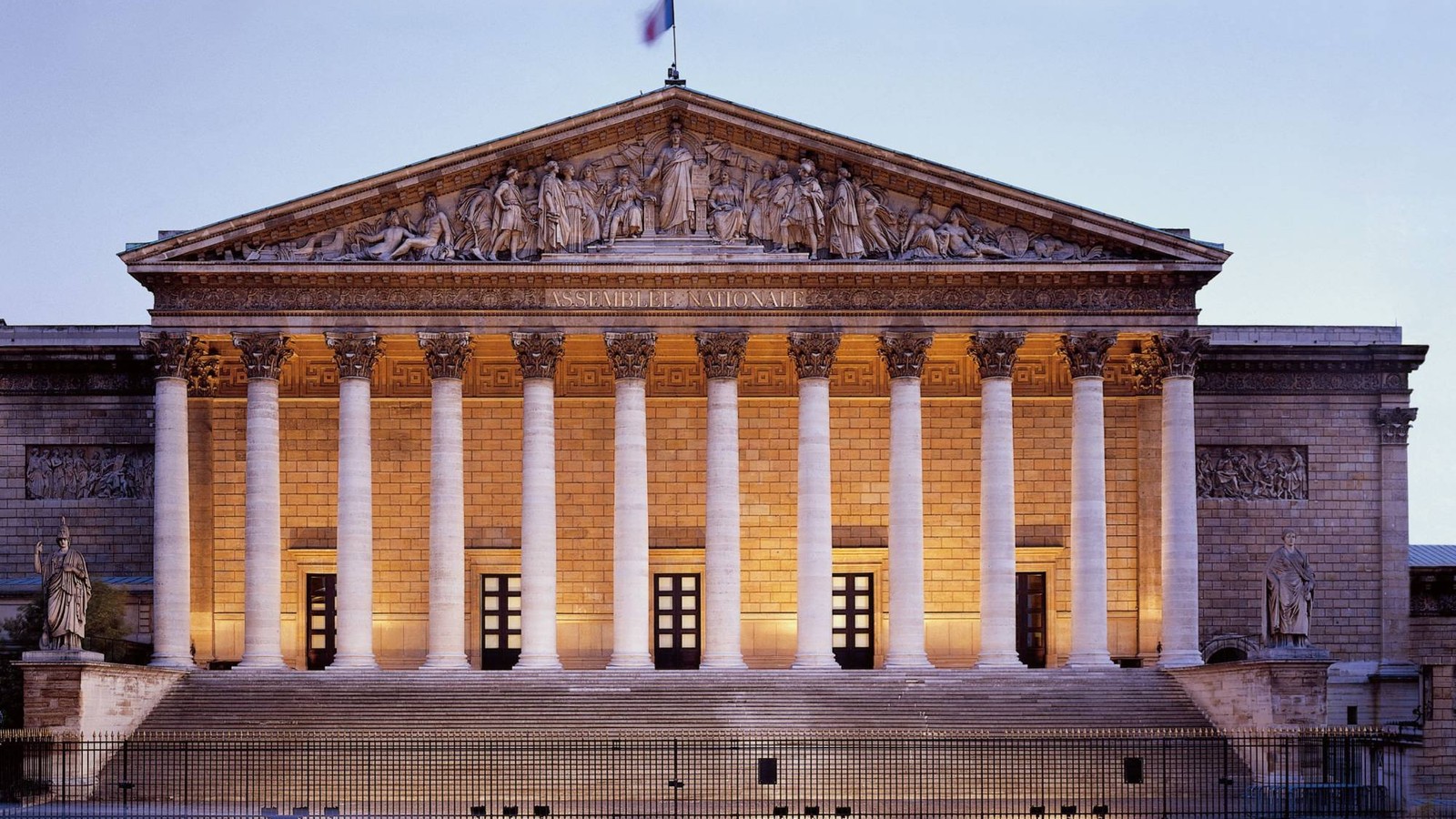 Façade illuminée de l'Assemblée nationale (Palais Bourbon) à Paris, au crépuscule, avec son fronton sculpté et sa colonnade éclairée.
