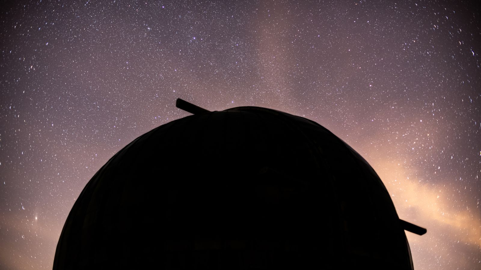 Silhouette d'un dôme d'observatoire astronomique sous un ciel étoilé, à l'horizon teinté de lueurs dorées.