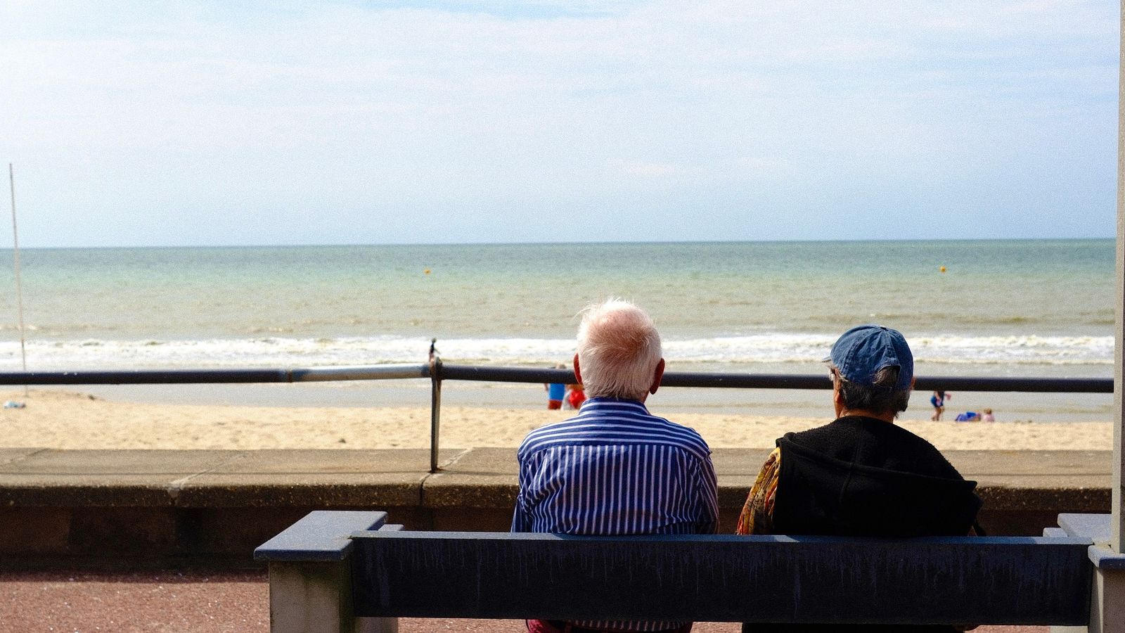 Couple de retraités assis sur un banc, de dos, face à la mer.