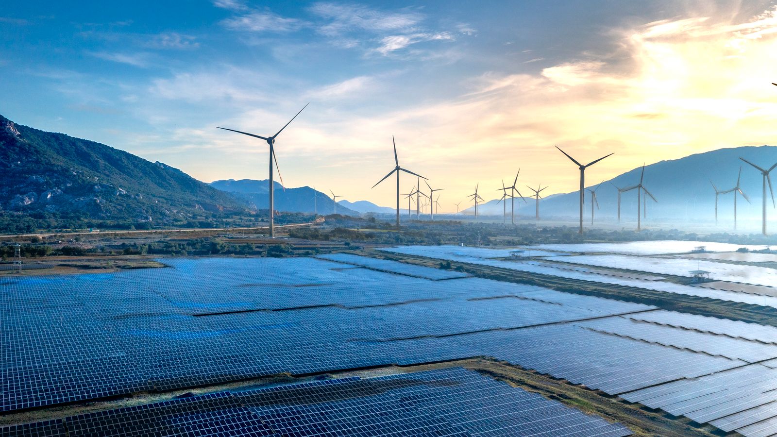 Éoliennes et panneaux solaires dans une vallée, au lever du soleil.