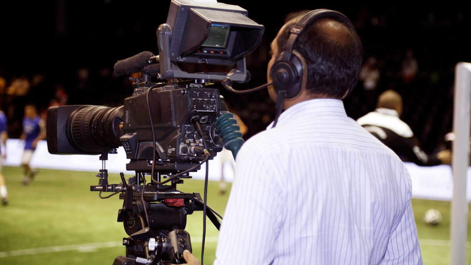 Un cameraman de télévision filme un match de football depuis le bord du terrain.