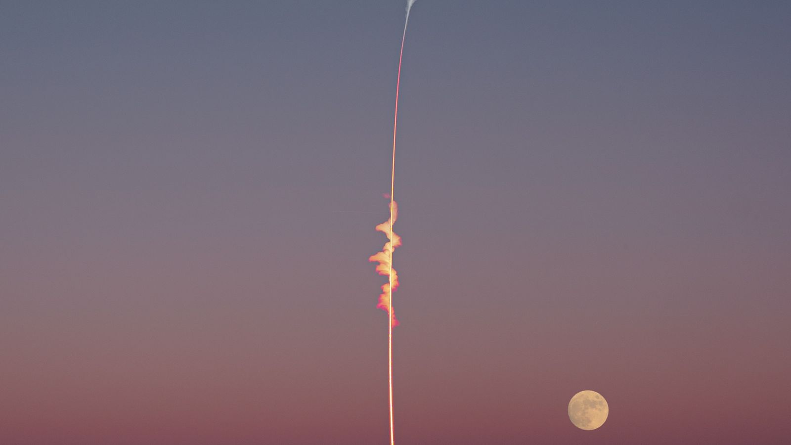 Une fusée s'élève dans le ciel du soir, avec la pleine lune visible à l'arrière-plan.
