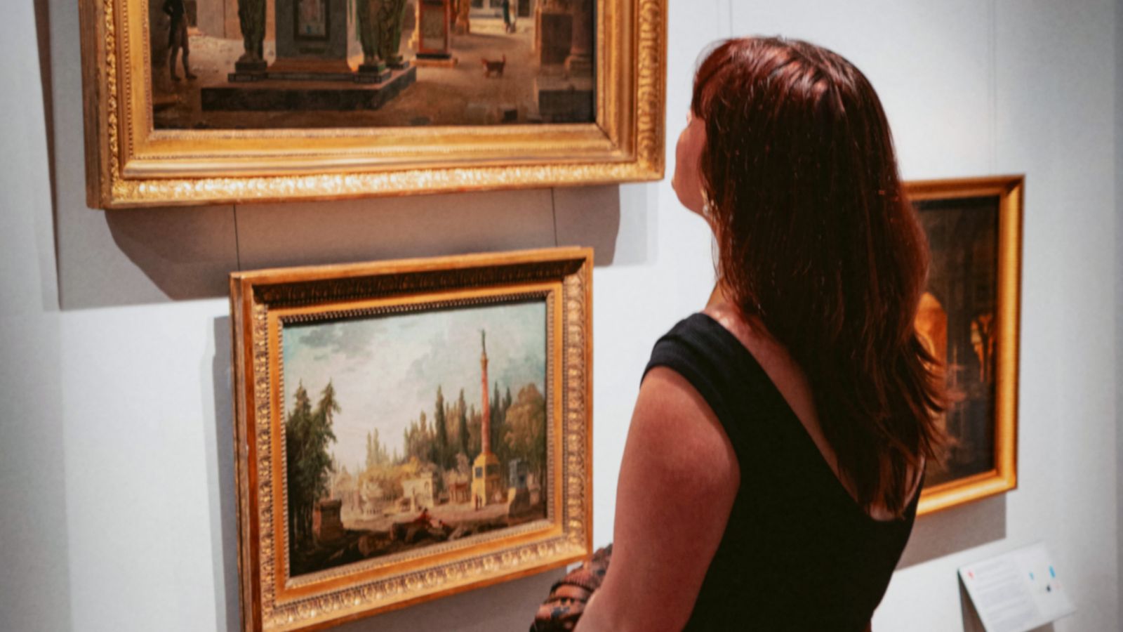 A visitor looks at richly framed paintings in an art gallery.