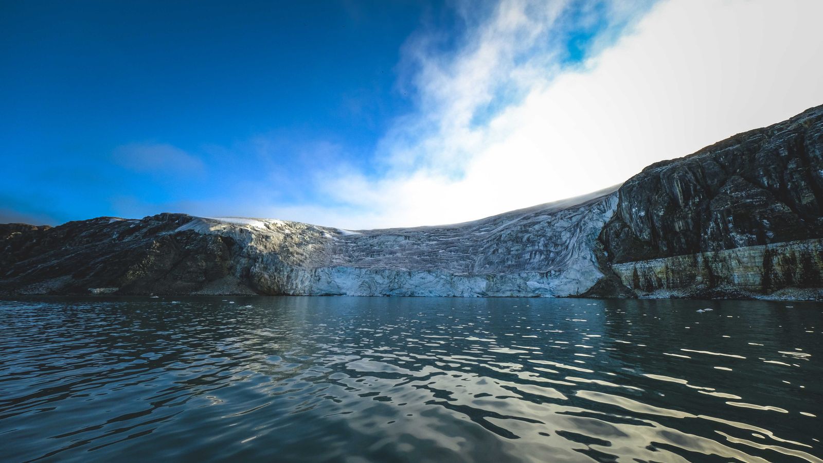 Un glacier arctique se jette dans une baie calme, sous un ciel dégagé.