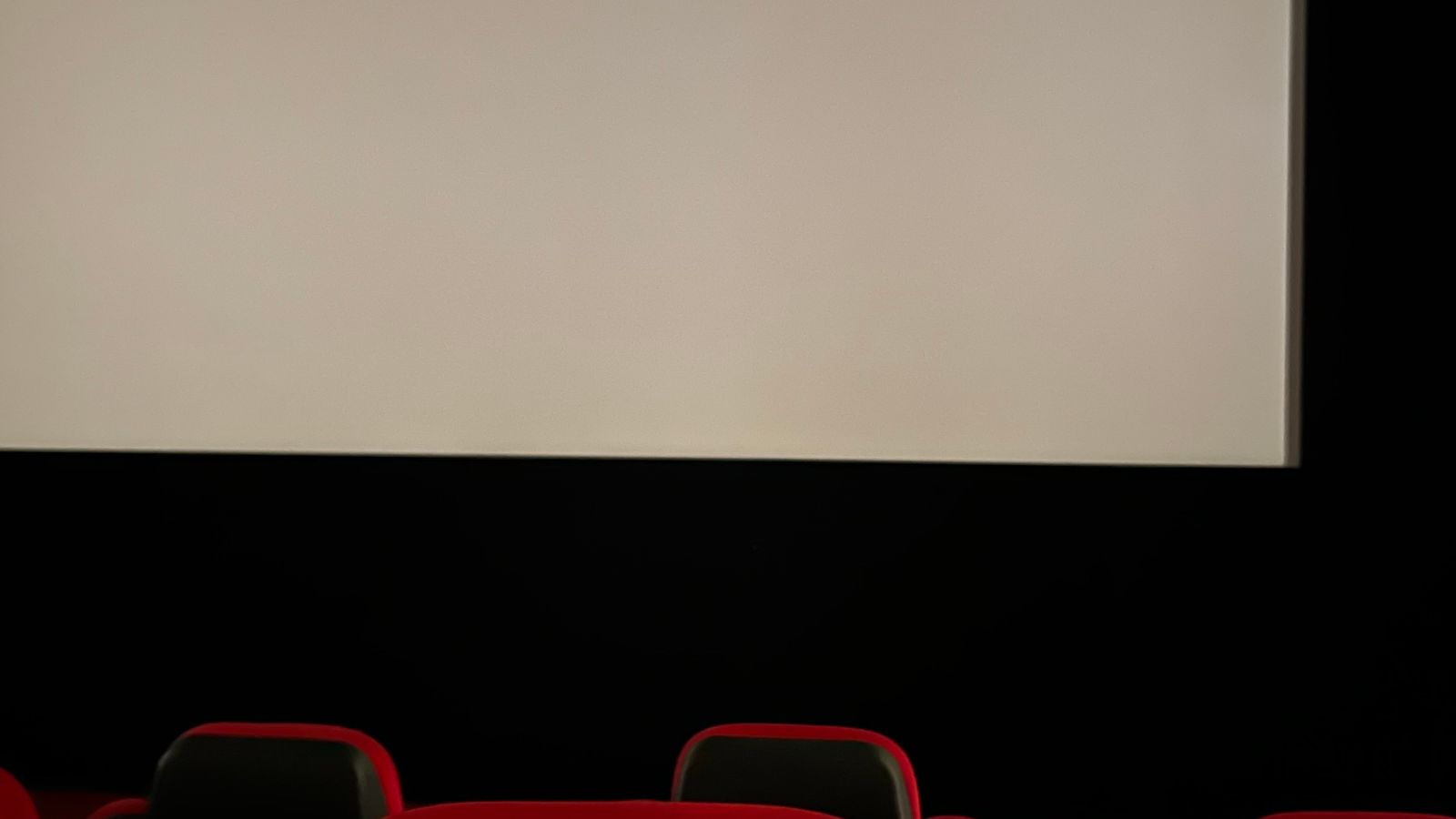 Salle de cinéma vide, écran allumé face à des rangées de sièges rouges.