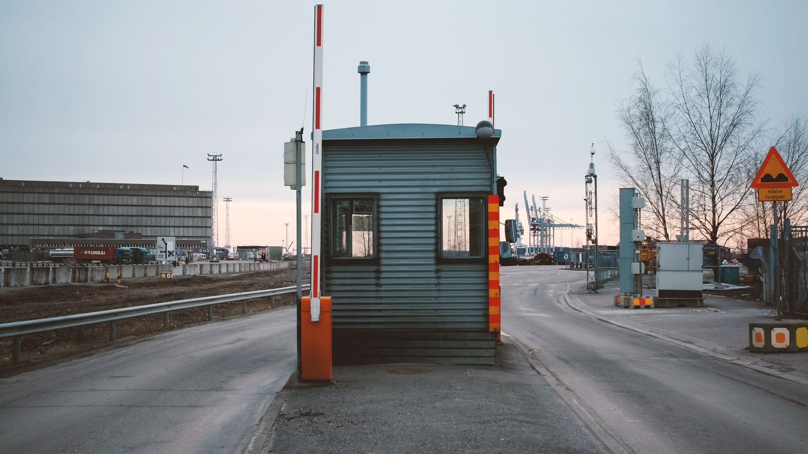 Une barrière de contrôle abaissée à l'entrée d'une zone portuaire, au crépuscule.