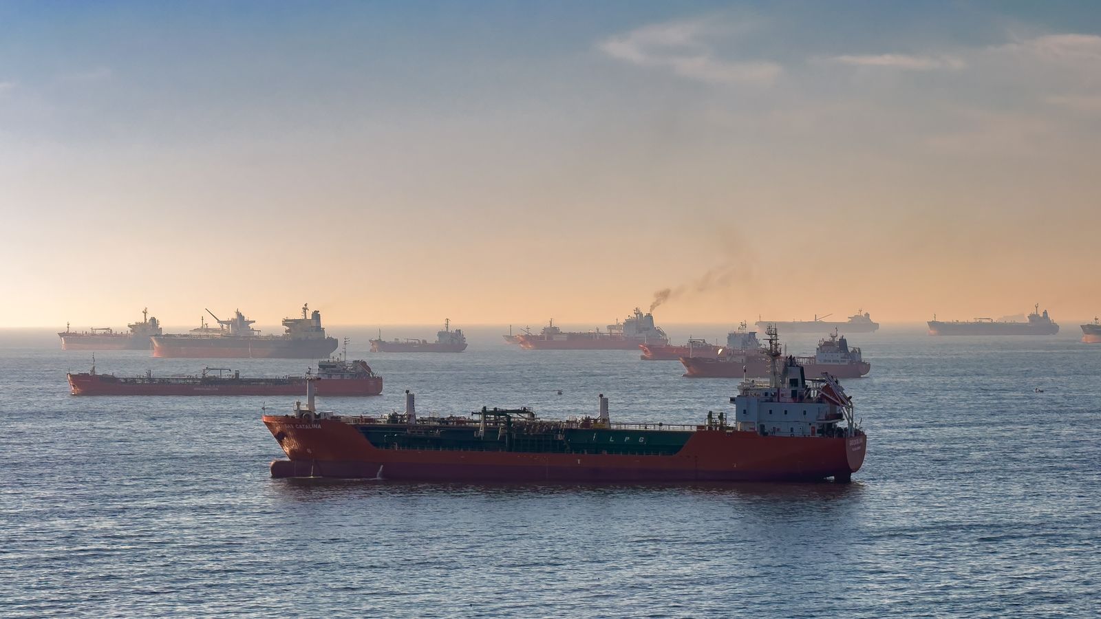 Une flotte de pétroliers et cargos à l'ancre au large, au coucher du soleil.
